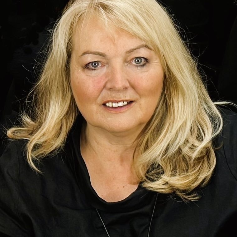 Eine Frau mit langen blonden Haaren, lächelnd vor einem dunklen Hintergrund.